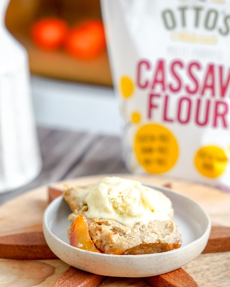 Gluten-free peach cobbler with vanilla ice cream on a plate. Bag of Otto's Naturals Cassava Flour in background