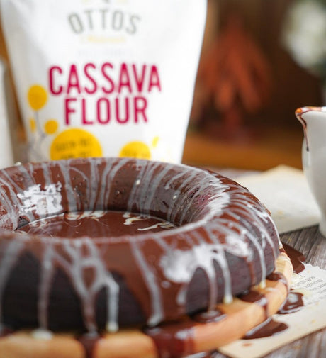 Grain-free chocolate zucchini cake with chocolate glaze and white chocolate drizzle. Bag of Otto's Naturals Cassava Flour in background