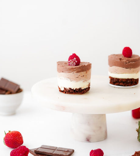 Grain-Free Triple Chocolate Mousse Cakes with Brownie Bases and Raspberries on top. Two mini mousse cakes on marble cake stand.