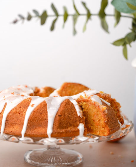 Grain-Free orange carrot bundt cake on cake plate. Drizzled in icing and garnished with orange zest