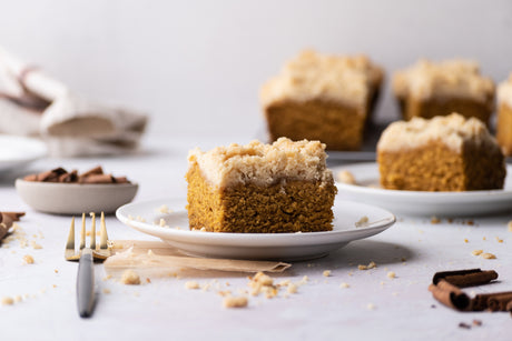 grain-free pumpkin coffee cake slice on plate with fork. More slices coffee cake in background on wire rack and other plate.