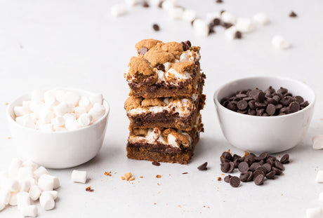 3 grain-free s'more cookie bars stacked, next to bowls of marshmallows and chocolate chips